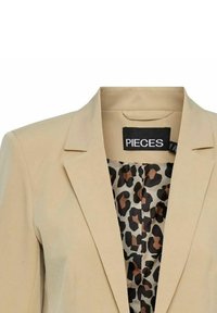 Blazer beige con un design su misura, revers a punta e fodera in stampa leopardata. Il tessuto appare liscio con una forma strutturata.