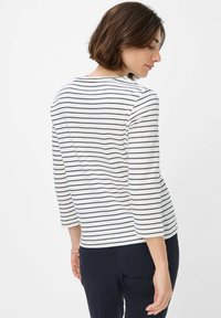 Gestreiftes Langarmshirt in Weiß und Marineblau. Verfügt über einen runden Halsausschnitt und mittellange Ärmel. Der Stoff erscheint weich und hat eine lässige Passform.