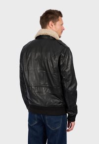 Černá kožená bunda s krémovým ovčím límcem, vybavená žebrovanými manžetami a hladkým povrchem. Obsahuje ramenní vycpávky a žádné viditelné vzory.