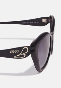 Lunettes de soleil noires avec une finition brillante. Monture carrée avec des verres foncés et un logo LIU-JO en or dans un design de papillon sur les branches.