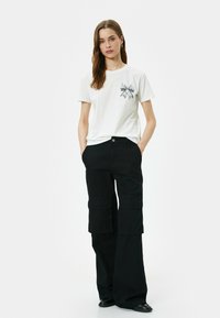 Hvid bomulds t-shirt med et sort sløjfe grafik på forsiden. Sammen med høj talje sorte cargo bukser med klaplommer.