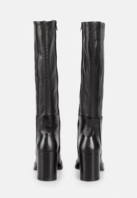 Bottes noires montantes en cuir lisse, avec fermeture éclair, couture verticale texturée et talons épais.