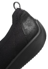 Black slip-on sneaker with knit fabric upper, textured heel panel, pull tab, and thick rubber sole shown in close-up.