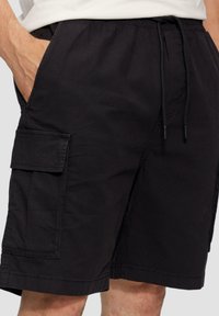 Shorts cargo noirs en tissu léger, dotés d'une taille avec cordon de serrage, de poches latérales et d'une poche utilitaire sur la jambe gauche.