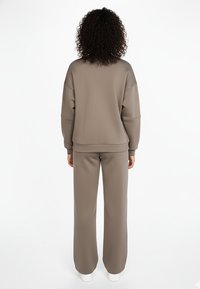 Brązowa bluza i dopasowane spodnie, wykonane z miękkiej, teksturowanej tkaniny. Luźny fason z opuszczonymi ramionami i elastycznymi mankietami.