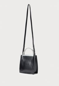 Borsa a tracolla in pelle nera con lunga tracolla regolabile e due manici curvi in metallo argento, in piedi su uno sfondo bianco uniforme.
