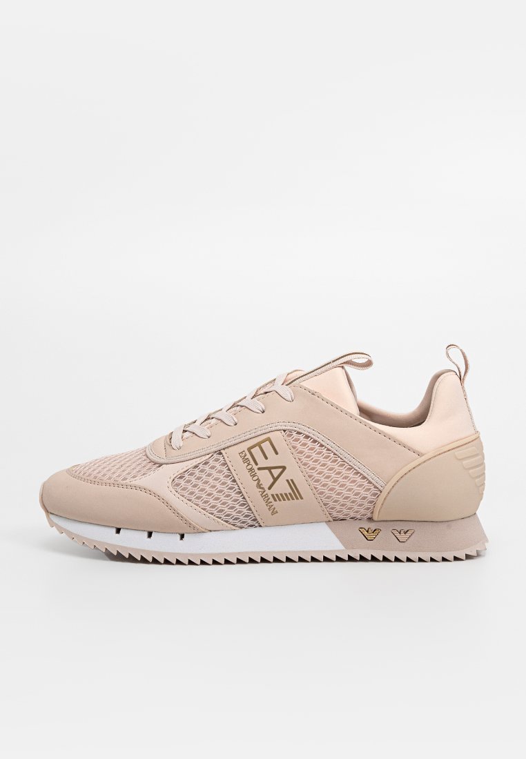 Zapatillas de color rosa claro con paneles de malla y acentos sintéticos. Presentan una suela blanca, cordones en tonalidad coincidente y un logo dorado en el lateral.