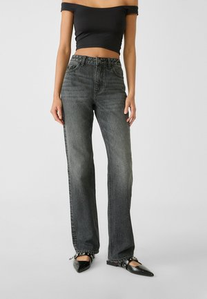 Dark gray high-waisted jeans with a straight leg fit, finished with pockets and a faded texture; accented with a black off-shoulder top and black flats.