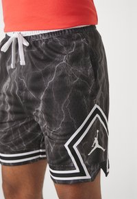 Schwarze Sportshorts mit einem Blitzmuster, aus atmungsaktivem Mesh. Verfügen über eine weiße Zugkordel und ein Jordan-Logo auf einem geometrischen Patch.