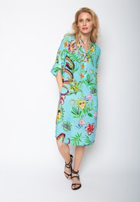 Türkises Kleid mit lebhaften floralen und abstrakten Mustern, kurzen Ärmeln, Knopfleiste und seitlichen Taschen. Leichter Stoff. Schlitz an den Seiten.