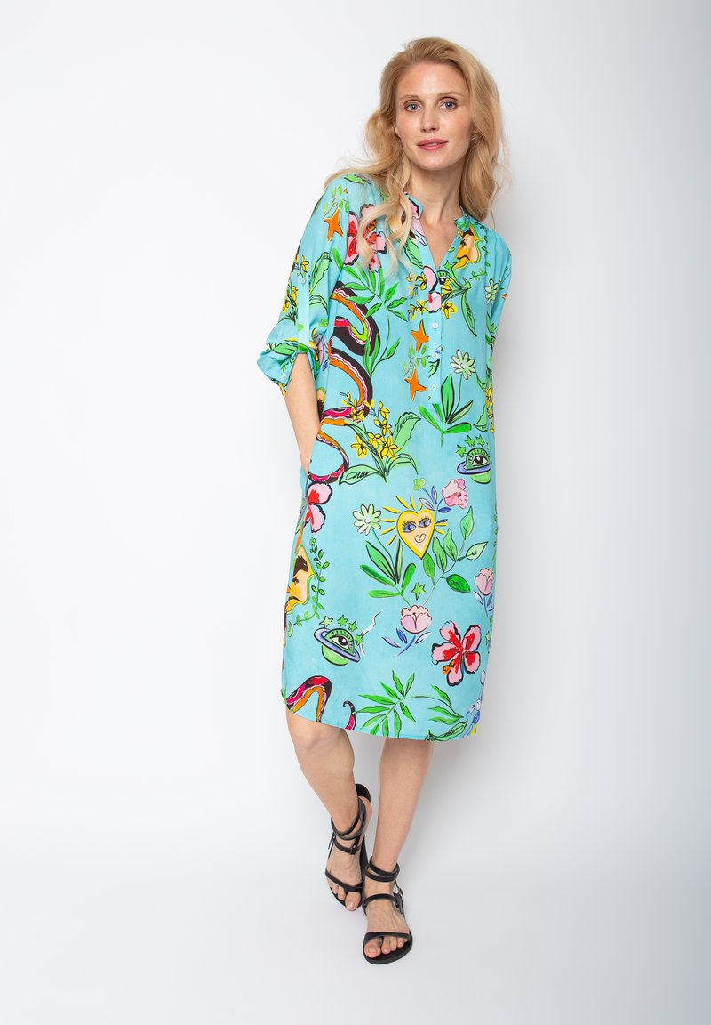 Türkises Kleid mit lebhaften floralen und abstrakten Mustern, kurzen Ärmeln, Knopfleiste und seitlichen Taschen. Leichter Stoff. Schlitz an den Seiten.