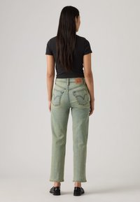 Πράσινο ξεθωριασμένο τζιν με ευθεία γραμμή, που διαθέτει λευκό κεντητό λογότυπο και πίσω τσέπες, συνδυασμένο με στενή μαύρη μπλούζα.