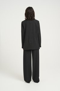 Completo nero a righe con giacca su misura e pantaloni a gamba larga, caratterizzato da una texture morbida e una leggera lucentezza.