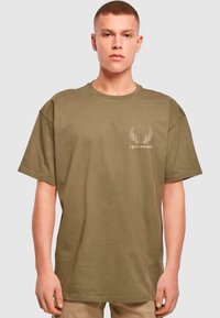 Olive green cotton t-shirt with short sleeves, ribbed texture, relaxed fit, featuring a white winged graphic logo on the chest.