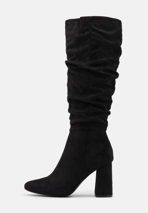 Bottes noires à hauteur de genou en doux daim, présentant un design loose, un bout pointu et un talon épais.