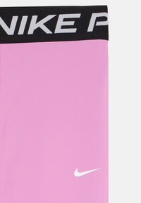 Tissu rose avec une ceinture noire affichant un texte partiel "NIKE P" en blanc et le logo swoosh de Nike en blanc près du coin inférieur droit.