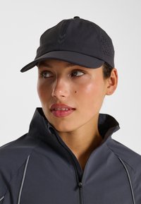 Schwarze Sportkappe mit strukturierter Form, vorne mit Logo, seitlichen Belüftungsöffnungen und passende dunkelgraue Jacke mit Reißverschluss.