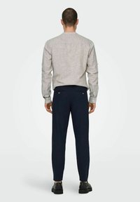 Camicia a maniche lunghe grigia chiaro in lino con polsini a bottone, abbinata a pantaloni classici blu scuro con tasche posteriori e una texture liscia.