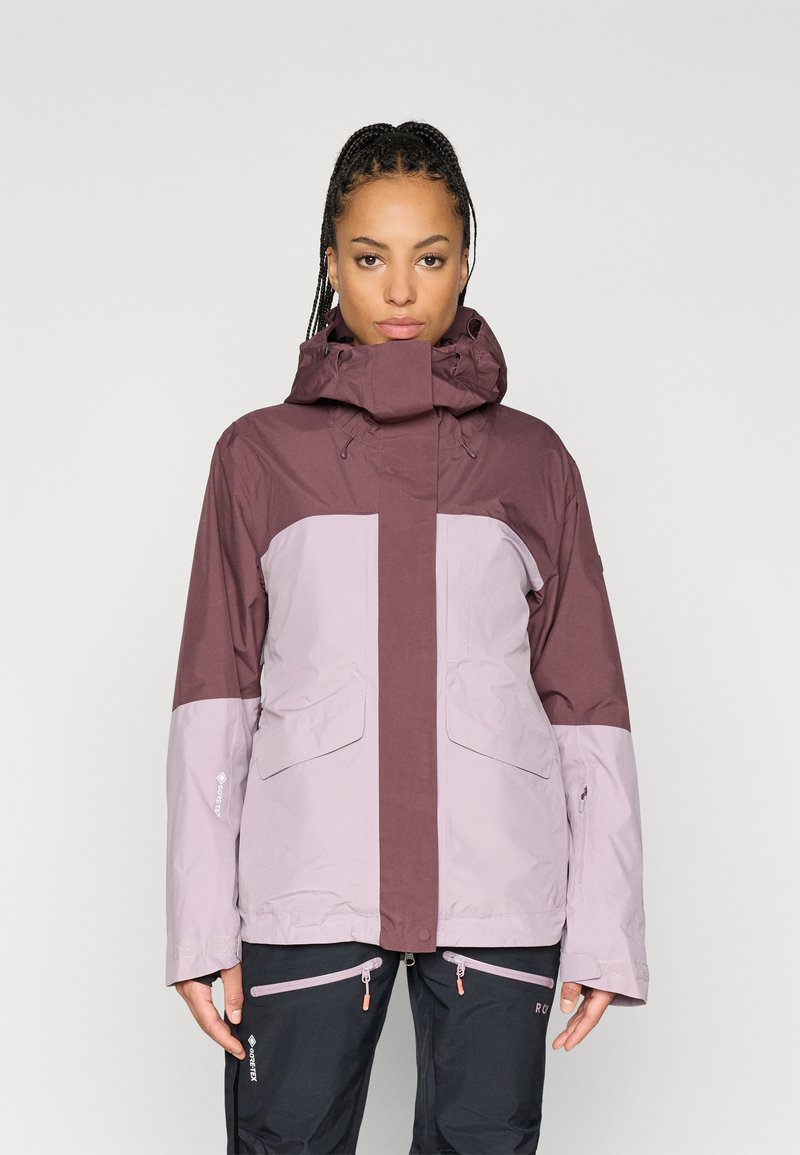 Vesitli vedenpitävä takki tummassa purppurassa ja vaaleassa laventelissa. Varustettu korkealla kauluksessa, säädettävällä hupussa ja etutaskuilla. Rakenteellinen kangas, tyylikäs muotoilu.