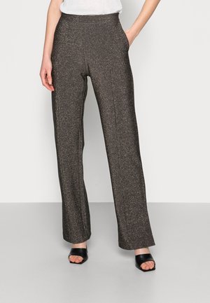 Vrouw draagt hoge taille, donkere glitterende wijde broek met voornaad, gecombineerd met zwarte open-toe sandalen met blokhak.