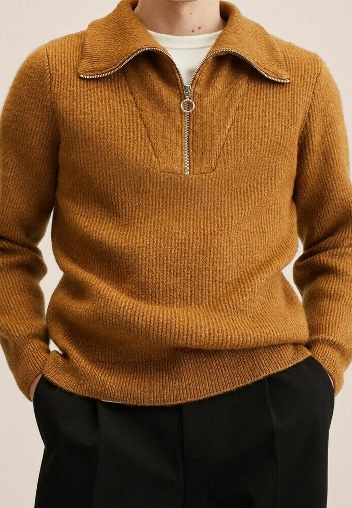 Strickpullover in einem warmen Senfton mit einem Reißverschluss an einem Stehkragen, gerippter Textur und einer taillierten Silhouette. Kombiniert mit dunkler Hose.