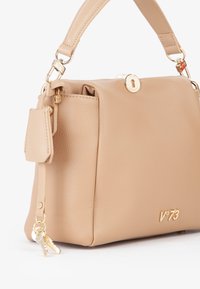 Borsa a mano in pelle beige con forma strutturata, hardware dorato, dettaglio con lucchetto e accent di portachiavi. Texture liscia e logo discreto.