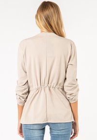 Beige Stretch-Bluse mit tailliertem Schnitt, dreiviertel Ärmeln und glatter Textur, mit rundem Ausschnitt und dezenten Rüschen-Details.