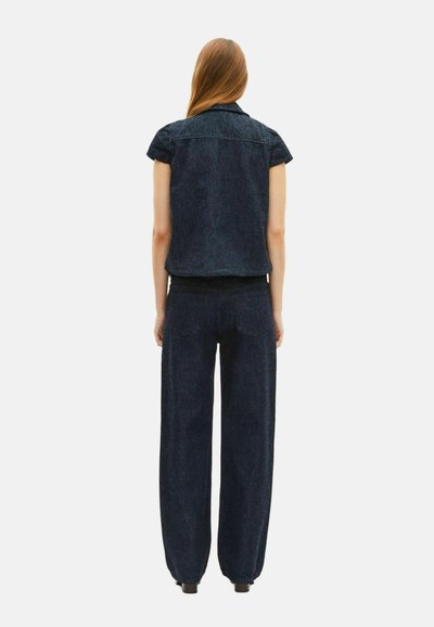 Giacca di jeans scura con maniche corte abbinata a pantaloni a vita alta e gamba larga. Texture liscia, dettagli di cucitura minimi e design semplice.