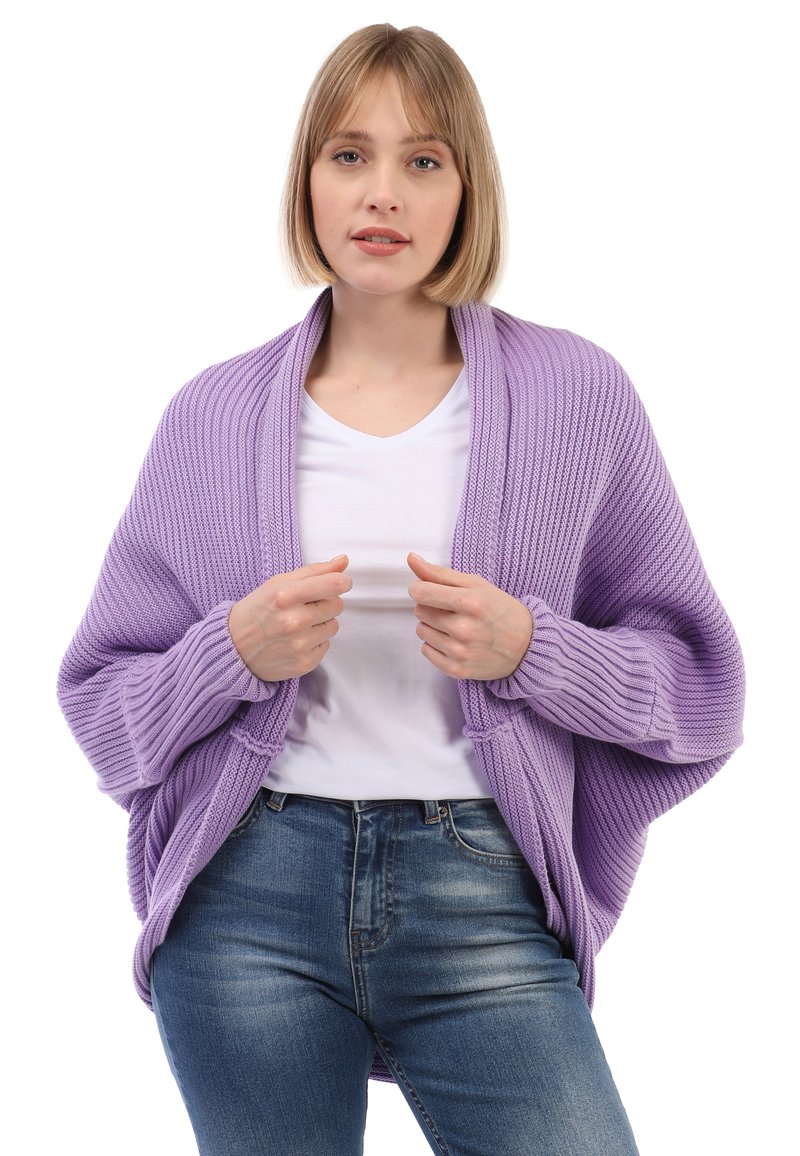 Lavender-farbene gestrickte Strickjacke mit gerippter Textur, offener Vorderseite und übergroßen Ärmeln, getragen über einem weißen Hemd und kombiniert mit blauen Jeans.