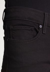 Jeans de mezclilla negros que cuentan con un bolsillo frontal con costuras visibles y un acento de botón de metal. Textura suave y diseño ajustado.