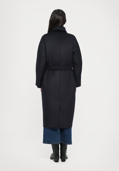 Navy wool coat with a belt, featuring a wide collar, back vent, and long sleeves, paired with blue denim wide-leg pants and black boots.