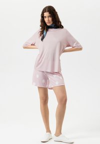 Haut rose pâle à manches courtes avec une coupe ample, associé à un short rose à grands pois blancs. Des baskets blanches complètent le look.