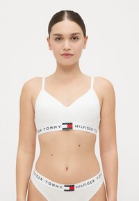 Witte bralette met dunne bandjes, V-hals ontwerp en logo band met rode, witte en blauwe accenten. Glad, rekbaar materiaal.