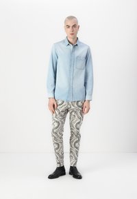 Denim skjorte med knapper i lys blå, med en brystlomme; kombinert med kremfargede bukser med et svart paisleymønster; svarte ankelstøvler.
