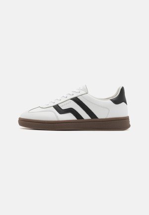 White leather sneakers with black diagonal stripes, round toe, flat brown rubber sole, and lace-up front.