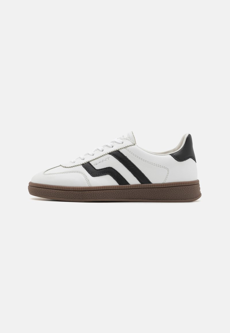White leather sneakers with black diagonal stripes, round toe, flat brown rubber sole, and lace-up front.