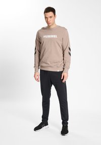Light beige sweatshirt with "HUMMEL" logo, black accents on sleeves, paired with black athletic pants and black sneakers.