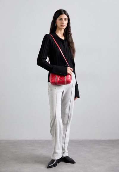 Schwarzes, geripptes Langarmshirt, graue Sweatpants mit seitlichen Streifen und eine rote patentierte Leder-Crossbody-Tasche. Schwarze spitze Schuhe runden den Look ab.