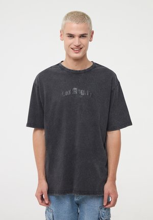T-shirt in cotone nero oversize con una stampa sbiadita che recita "Los Angeles". Presenta un collo tondo e maniche corte, indossato da un modello.
