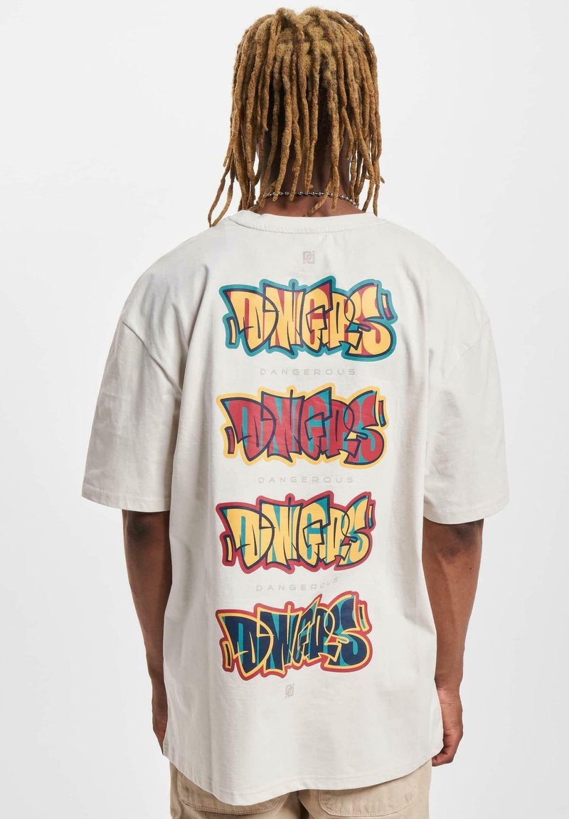 Světle béžové oversized tričko s výrazným, vícebarevným textem ve stylu graffiti na zadní straně, který opakovaně hlásá "DINGERS DANGEROUS".