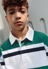 Pruhované polokošile zelené a bílé barvy s námořnickými detaily, vybavená složeným límcem a knoflíkovou légou, vyrobená z měkké, texturované látky.
