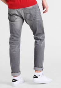 Jeans de mezclilla gris con un corte tapered, que presentan dobladillos enrollados y dos bolsillos traseros. Combinados con zapatillas blancas y un suéter rojo.