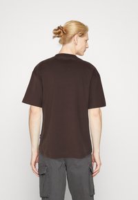 Brun bomulds t-shirt med korte ærmer og klassisk rund hals. Bagudsigten viser et enkelt design uden synlige mønstre eller grafik.
