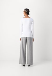 White long-sleeve top with a square neckline paired with wide, light grey, textured pants and black heeled shoes. Simple, minimalist design.