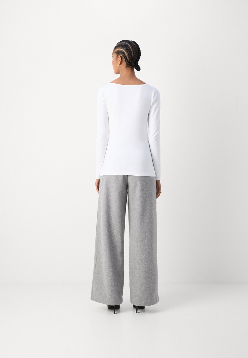 Top bianco a maniche lunghe con scollatura quadrata abbinato a pantaloni larghi grigio chiaro e testurizzati e scarpe con tacco nere. Design semplice e minimalista.