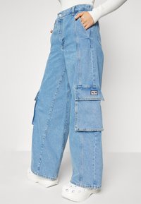Lyseblå, brede cargo bukser lavet af denim. Har store sidelommer og et mærke på venstre lomme. Tekstureret stof.