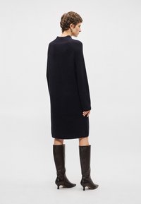 Πλεκτό φόρεμα μακρύ μανίκι σε σκούρο ναυτικό χρώμα με χαλαρή εφαρμογή και ριμπ ύφανση, συνδυασμένο με δερμάτινες μπότες έως το γόνατο σε σκούρο καφέ χρώμα.