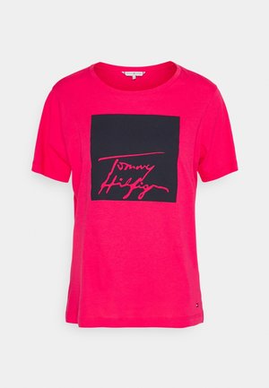 Lyserød T-shirt med korte ærmer, sort kvadrat og "Tommy Hilfiger"-signatur i pink skrift på fronten.