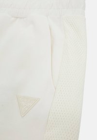 Hvide sweatpants med et tekstureret mesh-sidelag, elastisk talje og et gummilignende trekantslogo på frontlommen.