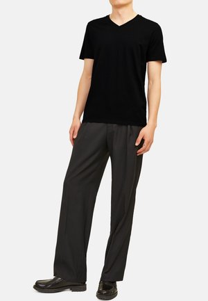 T-shirt noir à col en V associé à un pantalon ample gris foncé. Présente une texture de tissu lisse et un design minimaliste. Des chaussures noires complètent le look.